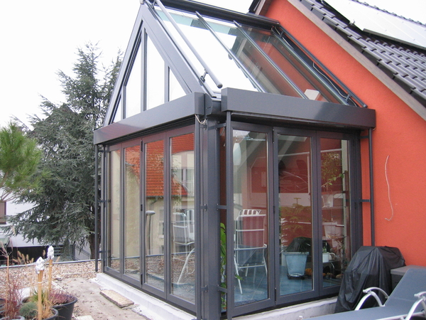 Moderner Wintergarten mit großen Glasfronten an einem Einfamilienhaus mit Solaranlage.