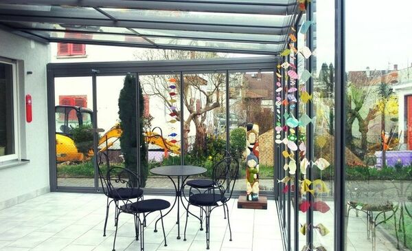 Moderner Wintergarten mit Glasfront, schwarzem Metalltisch und Stühlen sowie bunter Deko.