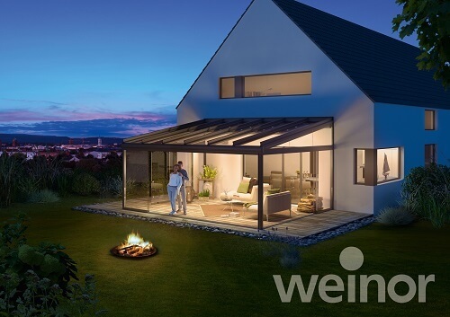 Modernes Einfamilienhaus mit beleuchtetem Wintergarten und Terrasse am Abend.