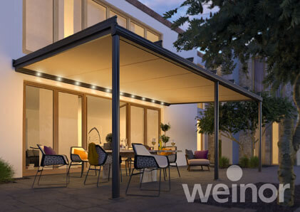 Moderne Terrassenüberdachung mit LED-Beleuchtung und Gartenmöbeln bei Sonnenuntergang.